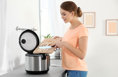 Young woman preparing mushrooms with modern multi cooker in kitchen