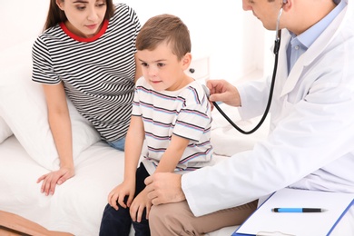 Children's doctor examining little patient with stethoscope at home