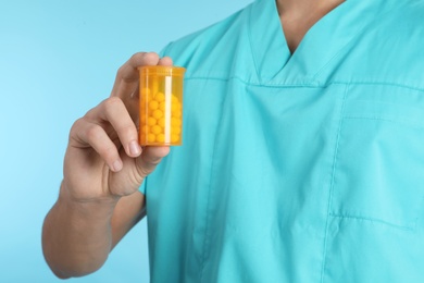 Male doctor holding pill bottle on color background, closeup. Medical object