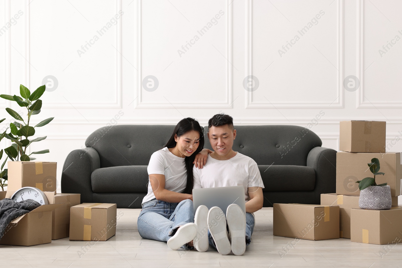 Photo of Happy couple with laptop on floor in their new apartment