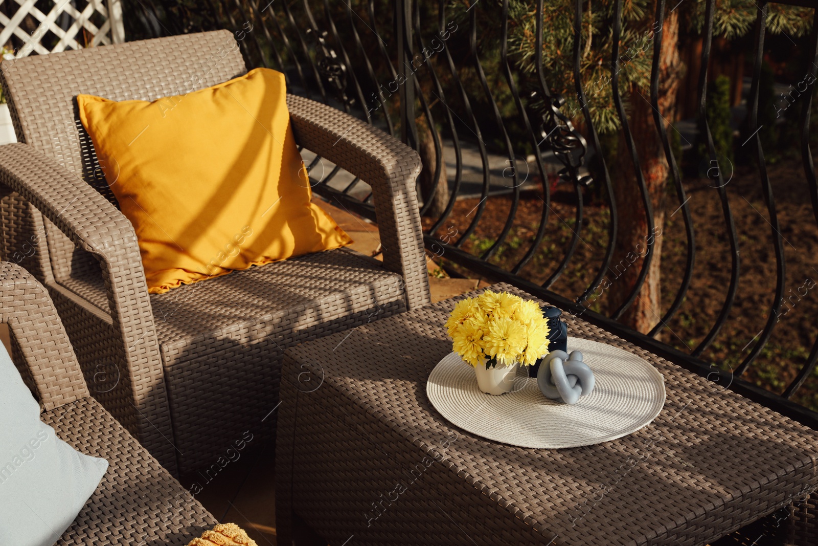 Photo of Orange pillow and yellow chrysanthemum flowers on rattan garden furniture outdoors