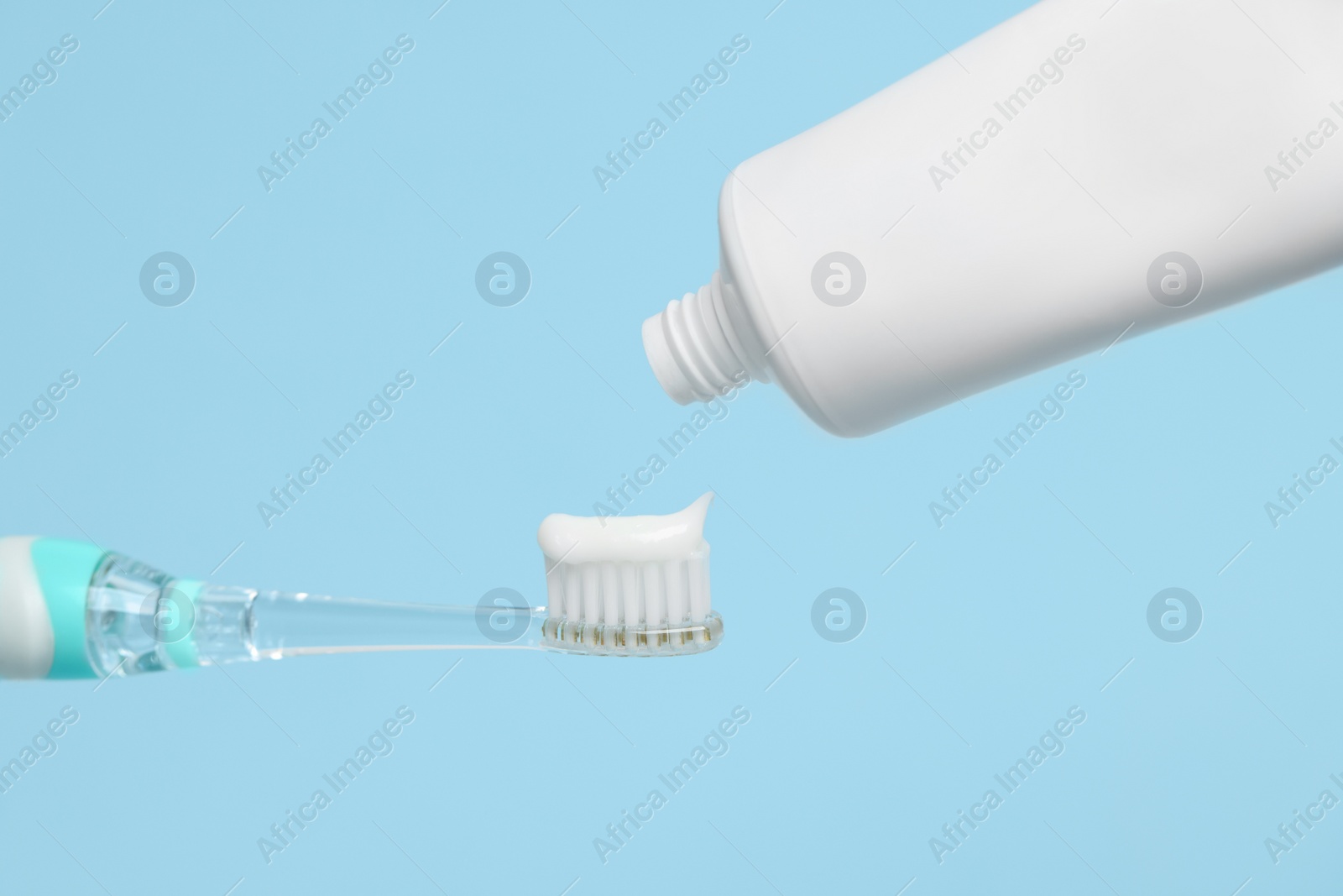 Photo of Electric toothbrush with paste on light blue background, closeup