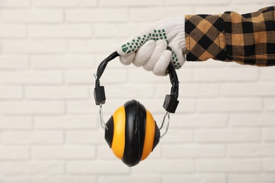 Photo of Worker holding safety headphones against white brick wall, closeup. Hearing protection device