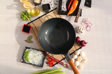 Photo of Wok, chopsticks and different products on white wooden table, flat lay