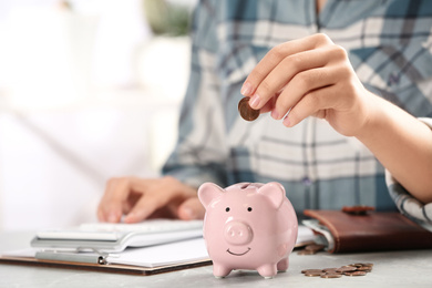 Woman putting money into piggy bank at table, closeup