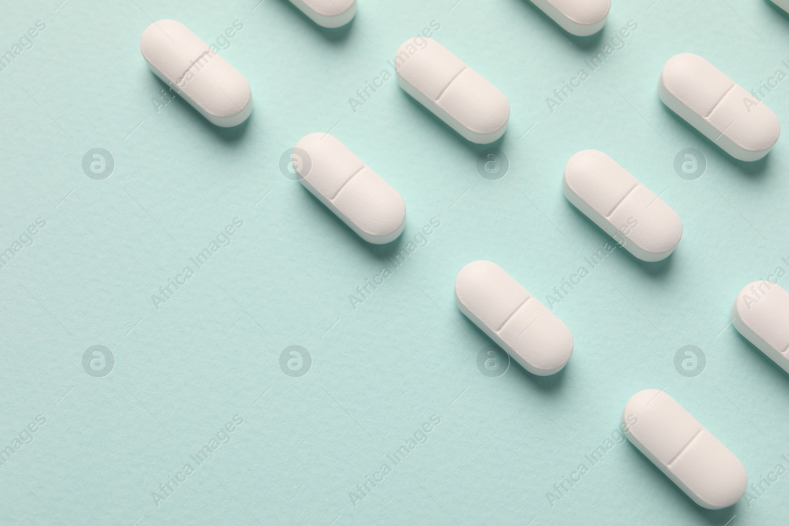 Photo of White pills on mint background, flat lay. Space for text