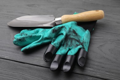 Pair of claw gardening gloves and trowel on grey wooden table, closeup