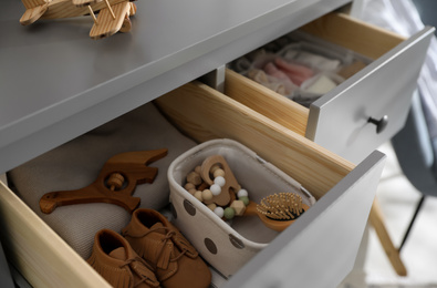 Photo of Open cabinet drawer with baby shoes and accessories in child room