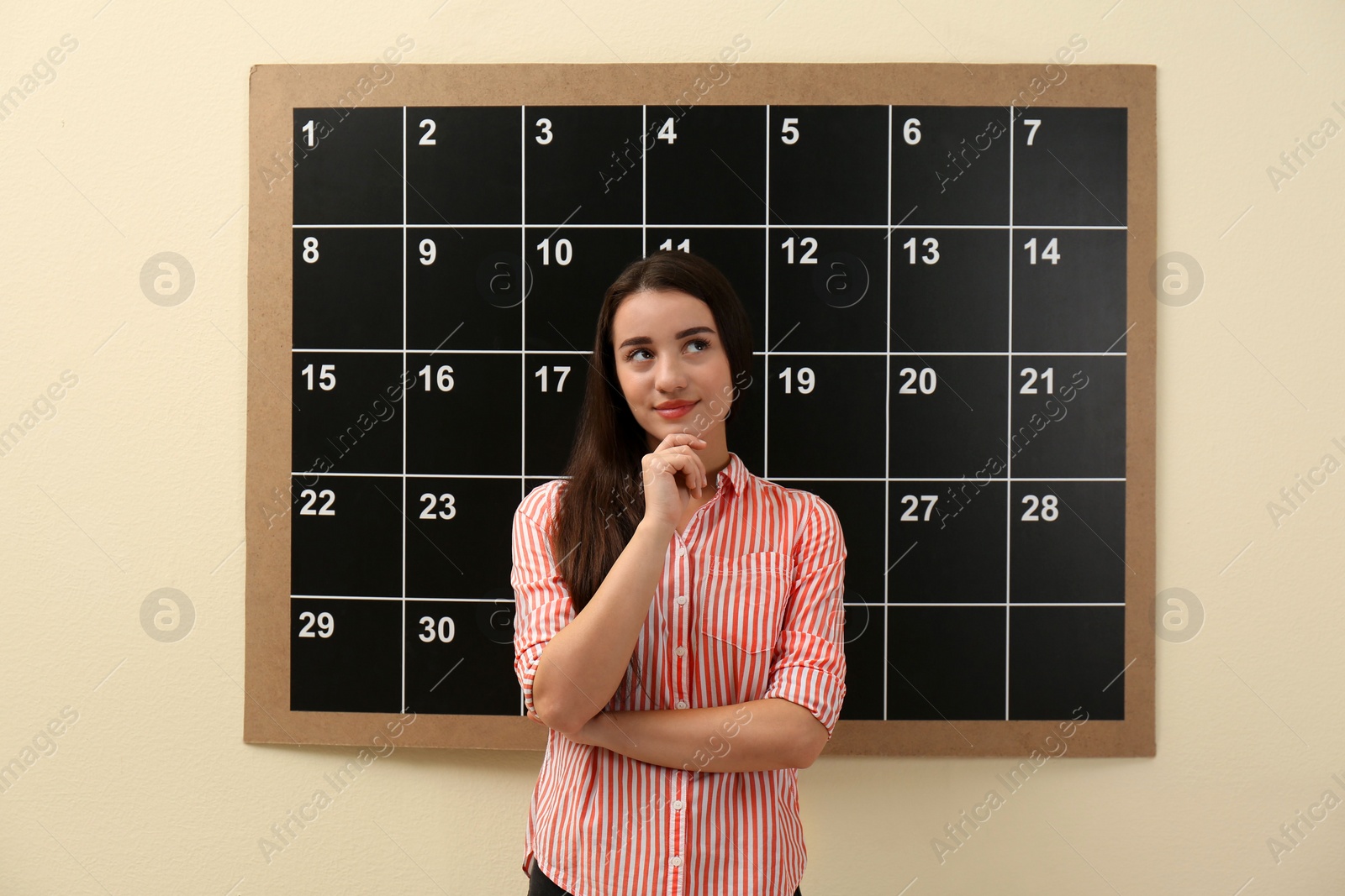 Photo of Young beautiful woman near board calendar  indoors