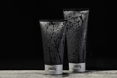 Photo of Wet tubes with men's cosmetic products on grey table against black background