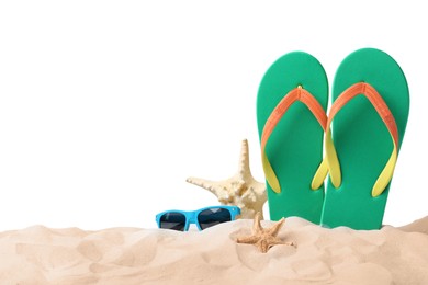 Green flip flops, starfishes and sunglasses on sand against white background