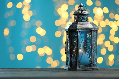 Photo of Traditional Arabic lantern on wooden table against light blue background with blurred lights. Space for text
