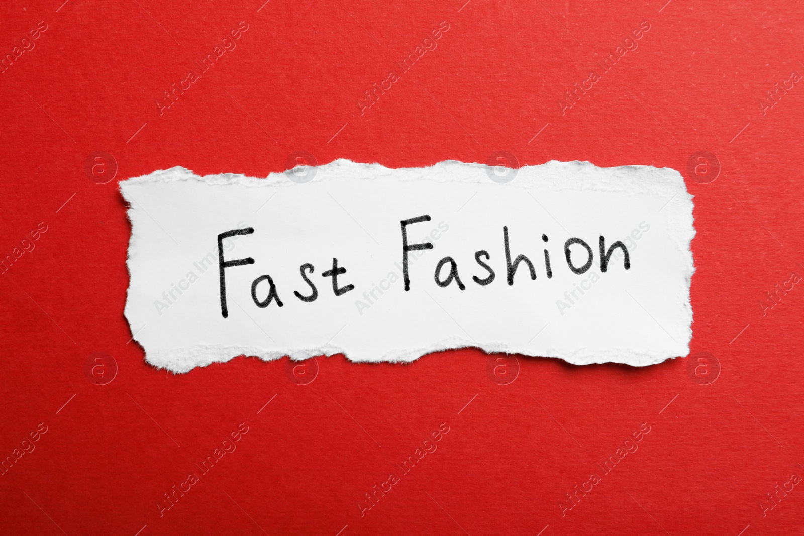 Photo of Torn piece of paper with phrase Fast Fashion on red background, top view