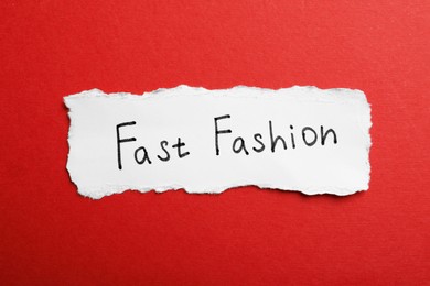 Photo of Torn piece of paper with phrase Fast Fashion on red background, top view