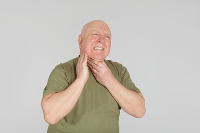 Photo of Senior man suffering from sore throat on light background. Enduring pain