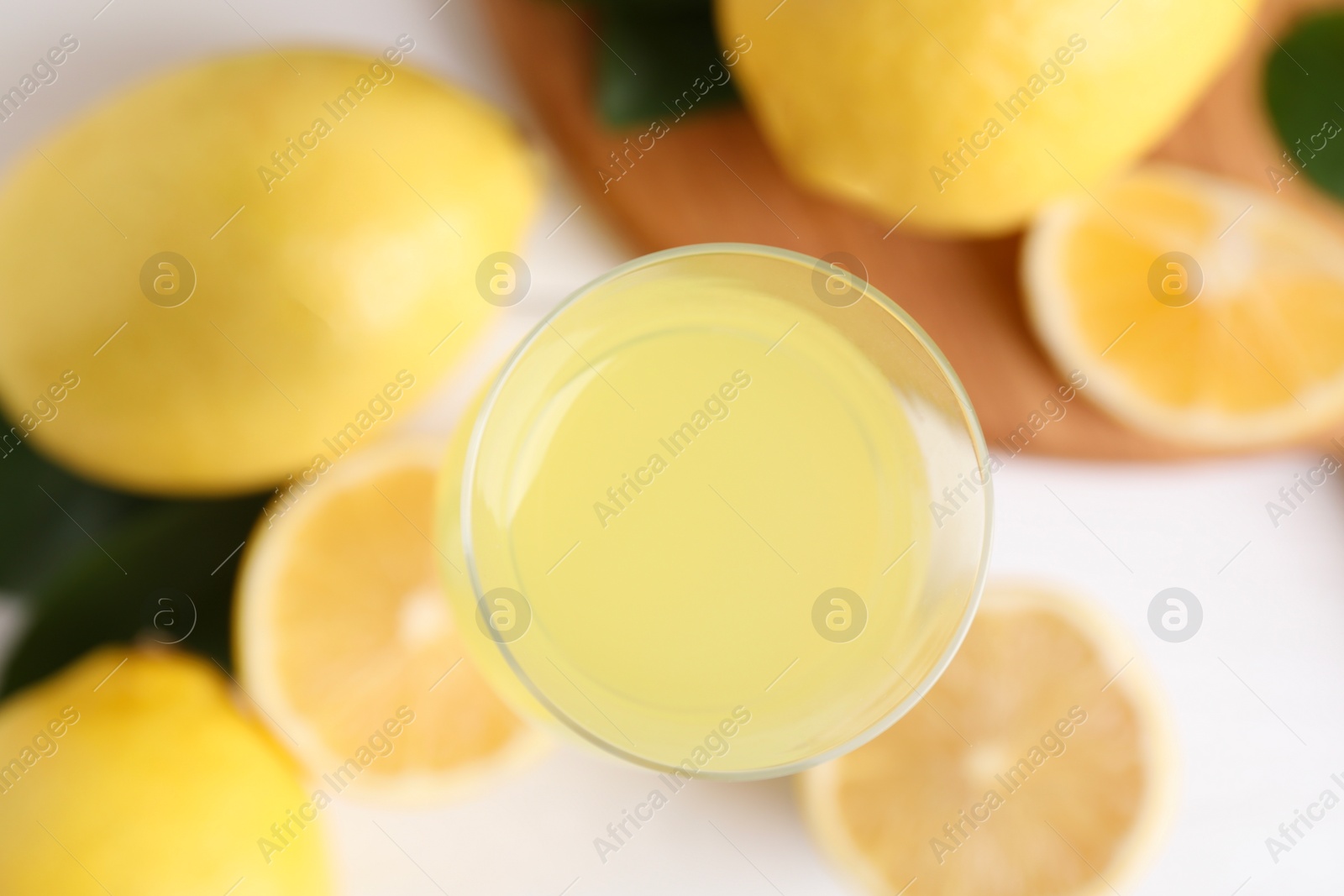 Photo of Liqueur glass with tasty limoncello, lemons and green leaves on table, top view