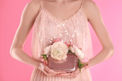 Photo of Woman holding elegant handbag with spring flowers on pink background, closeup