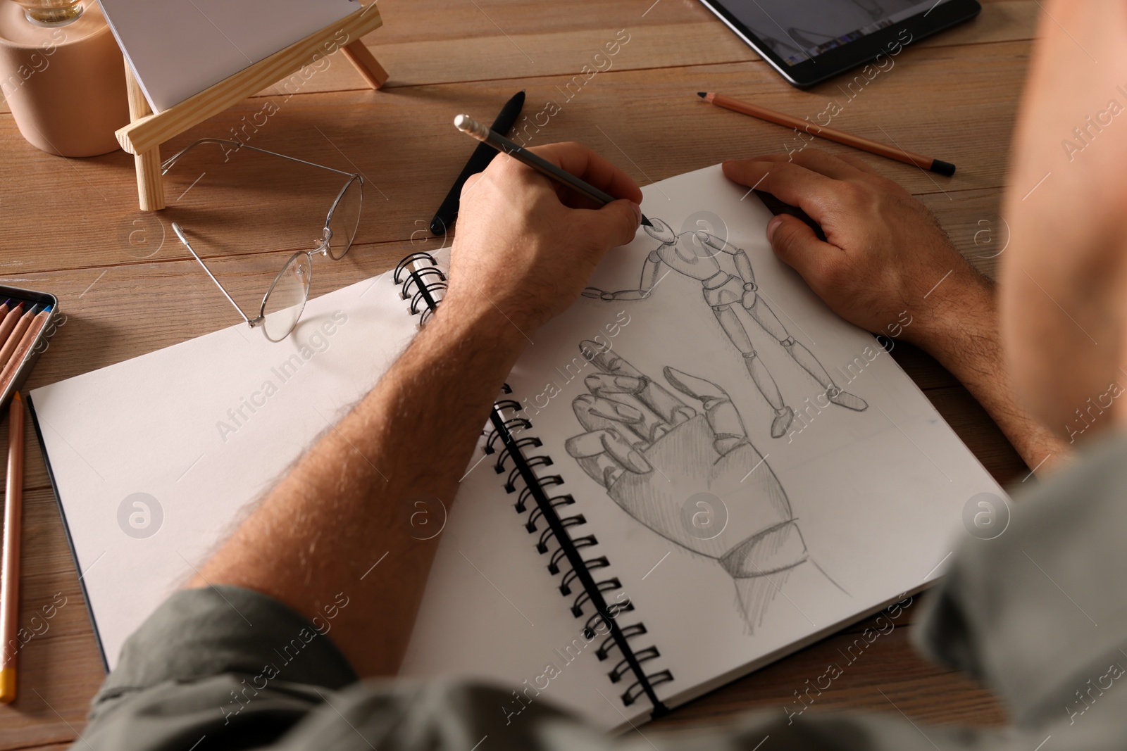 Photo of Man drawing in sketchbook with pencil at wooden table, closeup