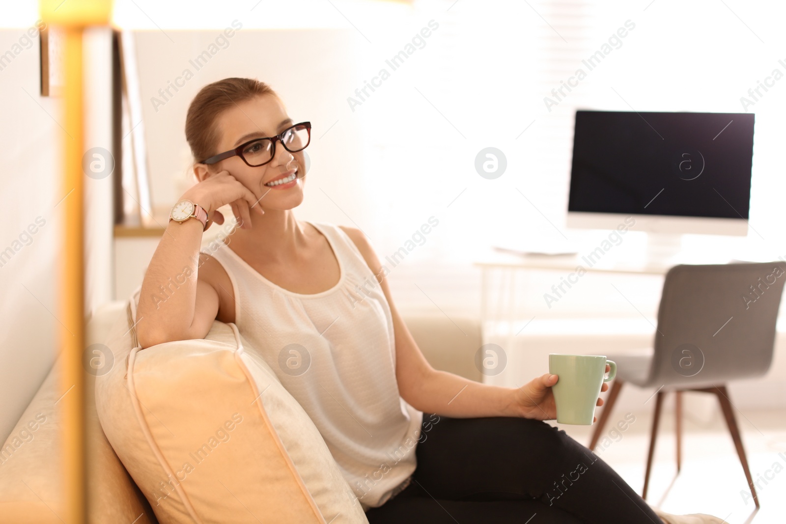 Photo of Young woman with cup of drink relaxing on couch in office