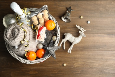 Photo of Wicker basket with gift set and Christmas decor on wooden table, flat lay
