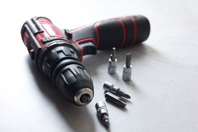 Photo of Modern electric screwdriver and bits on grey table, closeup