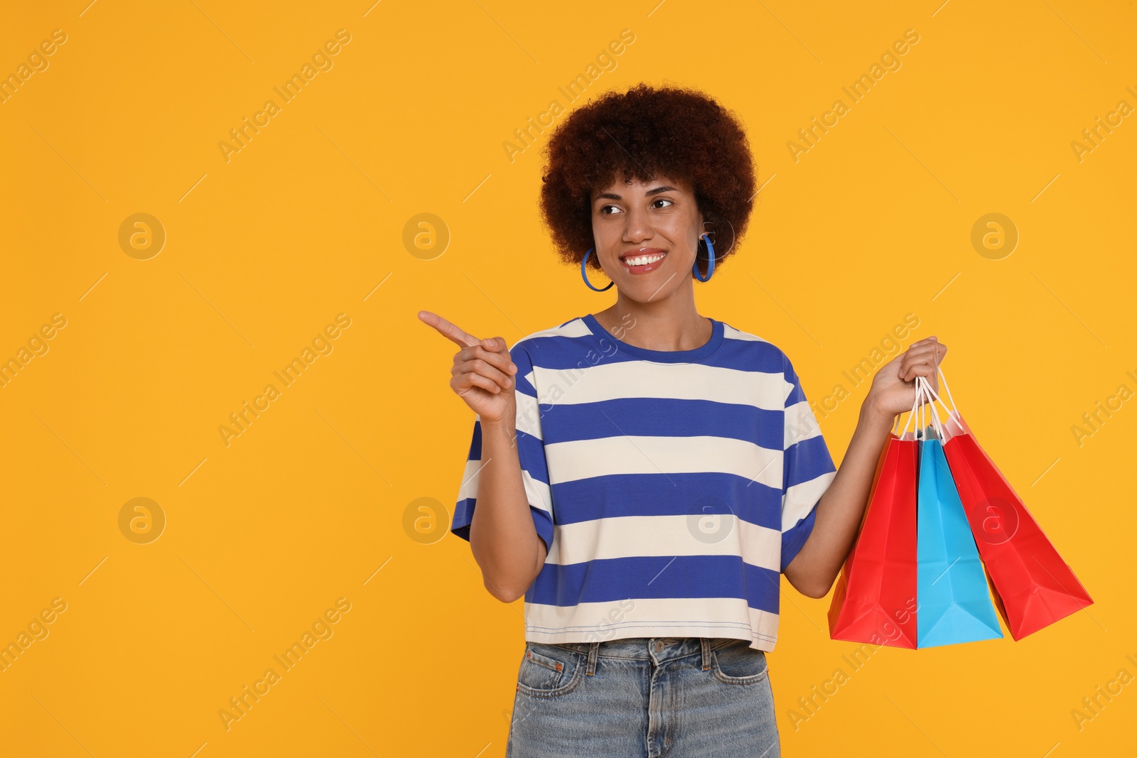 Photo of Happy young woman with shopping bags pointing at something on orange background. Space for text