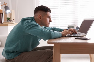 Photo of Man with poor posture using laptop at table indoors