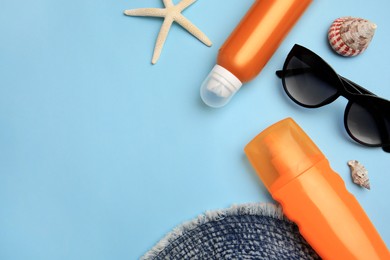 Flat lay composition with bottles of sunscreen on light blue background. Space for text