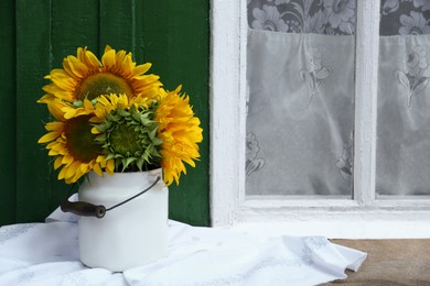 Bouquet of beautiful sunflowers in tin on wooden table near window outdoors