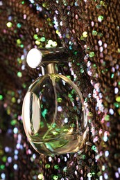 Photo of Luxury perfume in bottle on fabric with colorful sequins