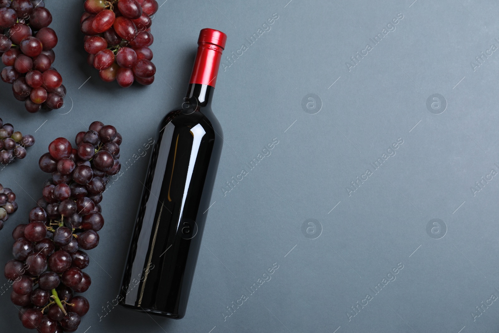 Photo of Fresh ripe juicy grapes and bottle of wine on grey background, flat lay. Space for text