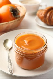 Photo of Delicious persimmon jam in glass jar served on white wooden table