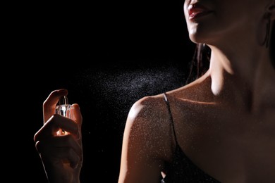 Woman spraying luxury perfume on black background, closeup
