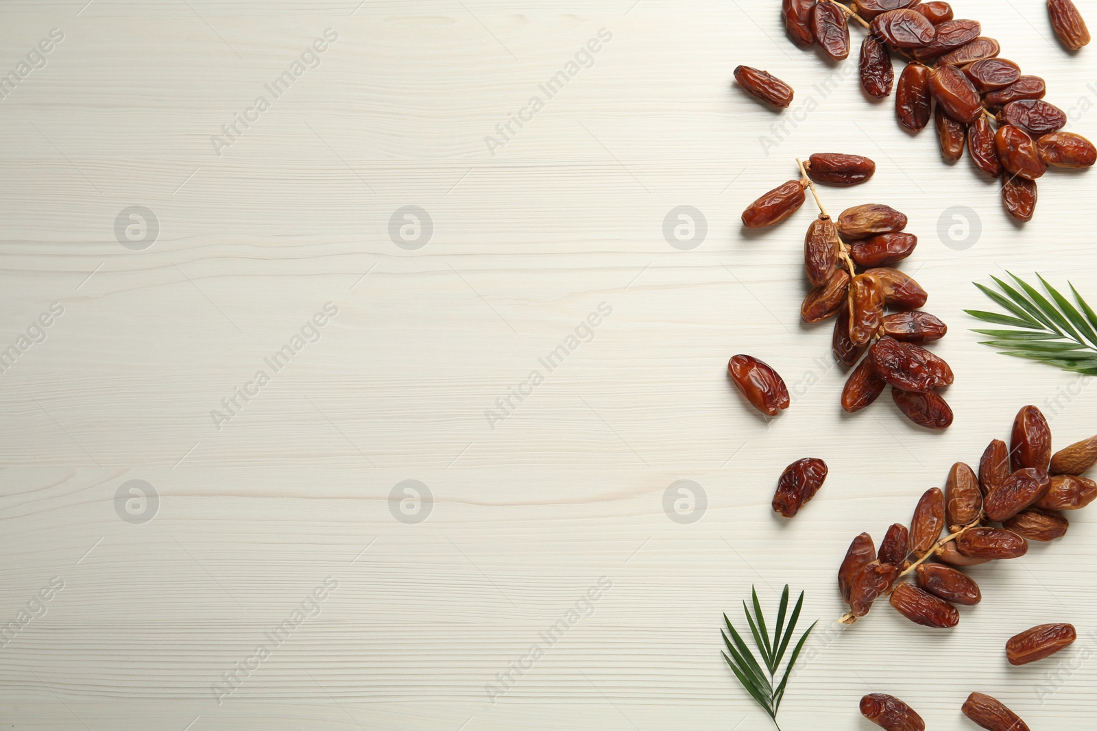 Photo of Tasty sweet dried dates with green leaves on white wooden table, flat lay. Space for text