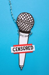 Photo of Card with word Censored, paper microphone and chain on light blue background, top view