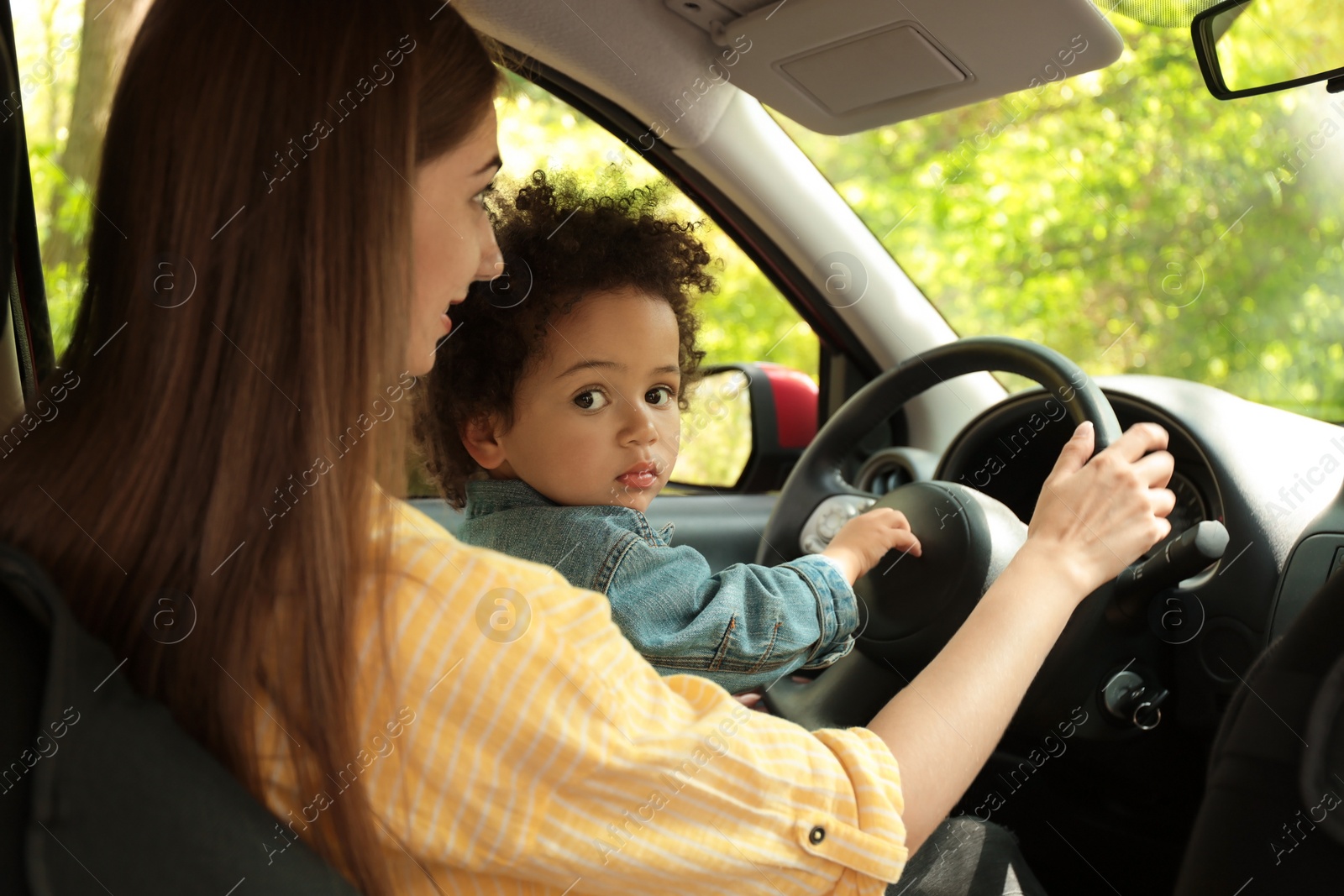 Photo of Mother with cute little daughter driving car together. Child in danger