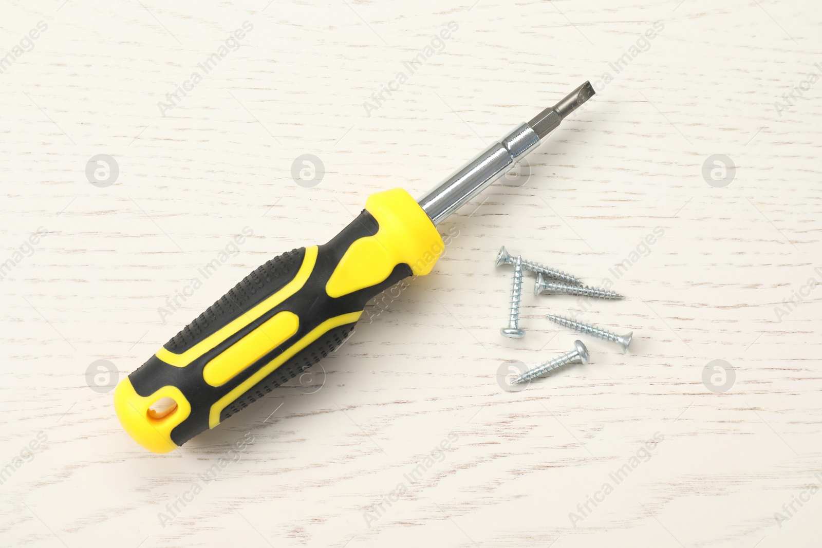 Photo of Screwdriver with yellow handle and screws on white wooden table, flat lay