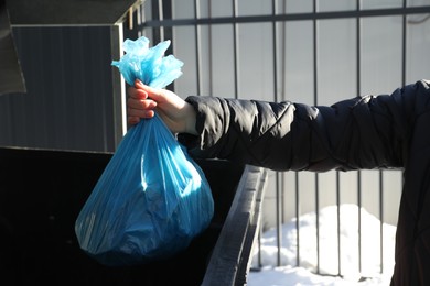 Photo of Woman throwing trash bag full of garbage in bin outdoors, closeup