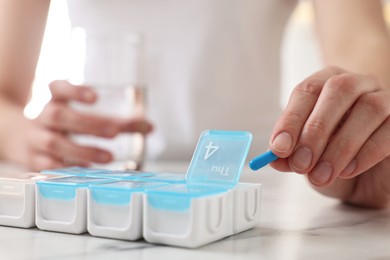 Photo of Woman with pills and organizer at white marble table, closeup