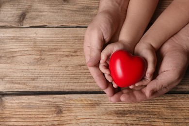 Father and his child holding red decorative heart at wooden table, top view. Space for text