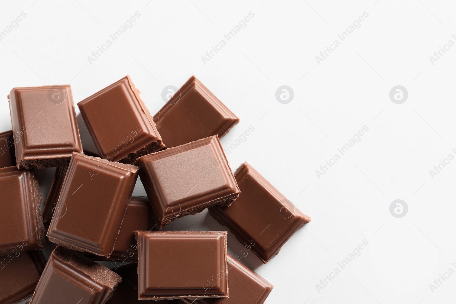 Photo of Pieces of tasty milk chocolate on white background, top view. Space for text