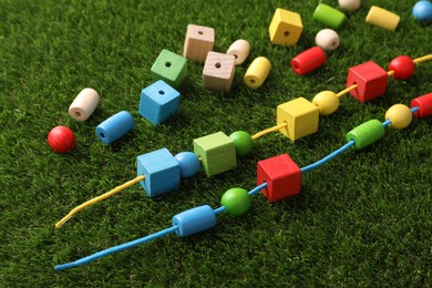 Photo of Wooden pieces and strings for threading activity on artificial grass. Educational toy for motor skills development