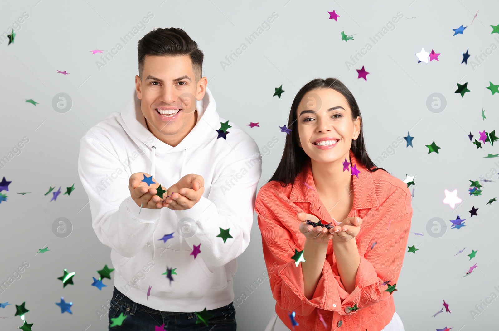Photo of Happy couple and falling confetti on light grey background