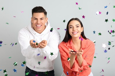 Happy couple and falling confetti on light grey background