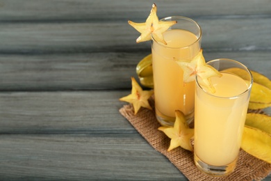 Photo of Delicious carambola juice and fresh fruits on grey wooden table. Space for text