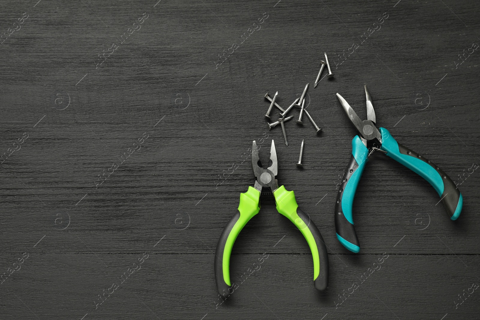Photo of Pliers and nails on black wooden table, flat lay. Space for text