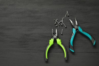 Pliers and nails on black wooden table, flat lay. Space for text