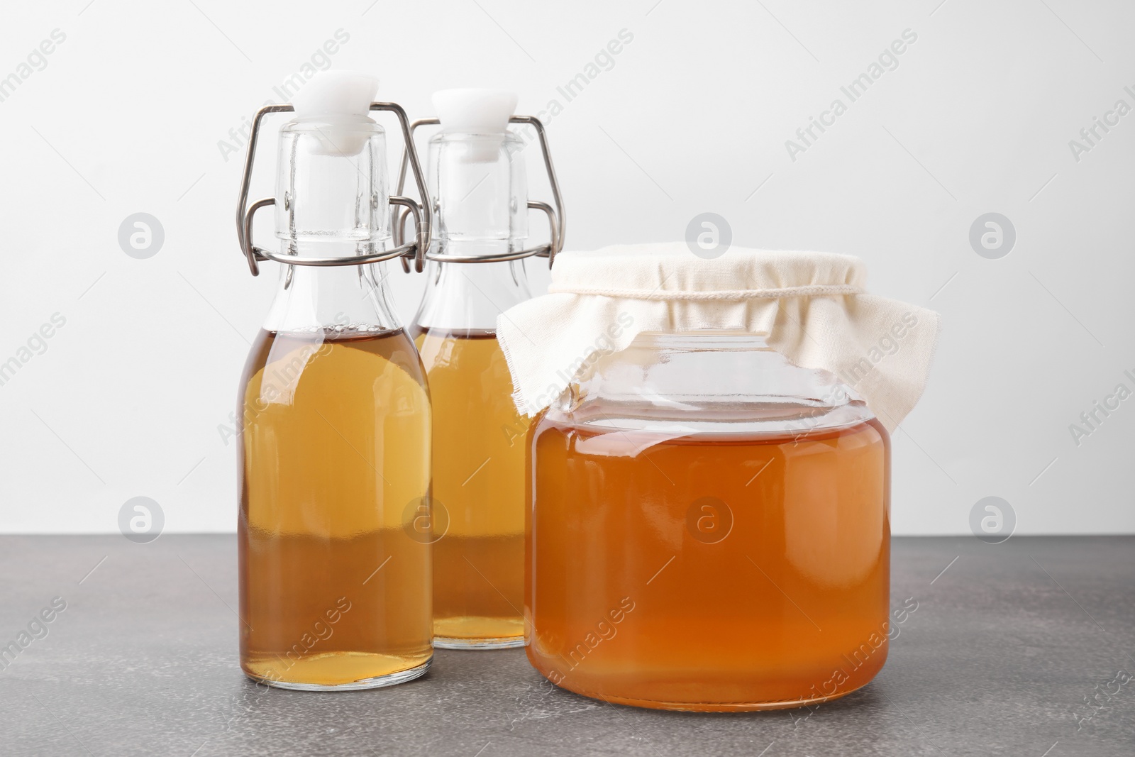 Photo of Homemade fermented kombucha in glass jar and bottles on grey table