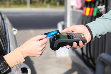 Photo of Woman sitting in car and paying with credit card at gas station, closeup