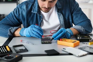 Photo of Technician checking broken smartphone at table in repair shop, closeup